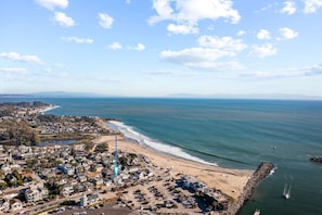 Vista aérea de un pueblo costero con playa, zona residencial y un faro.
