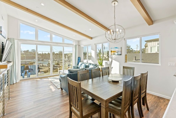 A spacious dining area with a wooden table and chairs, large windows, and a view of the outside.