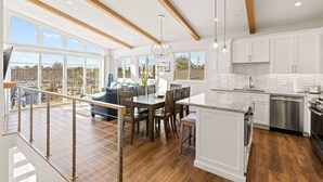 A modern kitchen with white cabinetry, a large island, and a dining area with wooden chairs. - Santa Cruz Harbor Vacation (Santa Cruz)