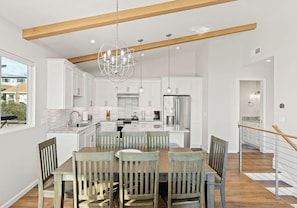 A modern kitchen with white cabinets, a wooden dining table, and a chandelier.