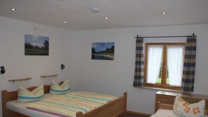Ein Schlafzimmer mit einem hölzernen Bett, zwei Kissen, einem Nachttisch und einem Fenster mit Vorhängen.