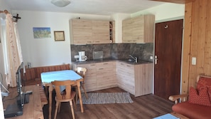 A compact living space with a kitchenette, a dining area with a table and chairs, a sofa, and a wooden door. - Krokus Apartment: 40 m², terrace, kitchenette, 1 bedroom, living room (Ruhpolding)