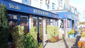 Un restaurant à la façade bleue, avec une enseigne indiquant qu’il sert des fruits de mer, et des tables en plein air agrémentées de plantes en pot.