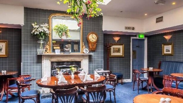 Une salle à manger d’hôtel avec des tables rondes, des chaises en bois, une cheminée et un grand miroir au mur.