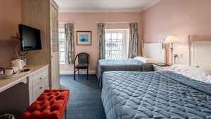 Une chambre d’hôtel avec deux lits, un bureau, une chaise, une télévision et une fenêtre avec des rideaux.