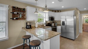A modern kitchen with white cabinets, a stainless steel refrigerator, a granite countertop, and a coffee maker.
