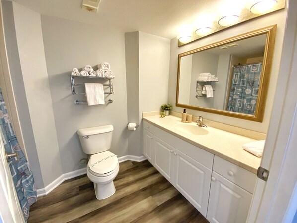 A bathroom with a toilet, sink, vanity, and a large mirror.