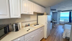 Una cocina compacta con armarios blancos, microondas integrado, cafetera y refrigerador.