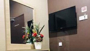 A compact room with a wooden desk, a chair, a television mounted on the wall, and a small potted plant on the desk. - Highway Times Inn (Ipoh)