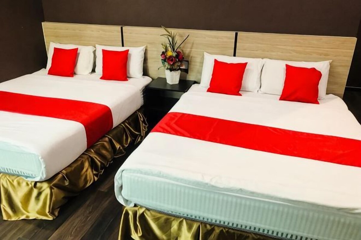 Two twin beds with red and white bedding, a wooden headboard, and a small table with a vase of flowers.