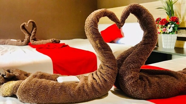 A hotel room with two beds, one with a red blanket and a heart-shaped towel arrangement. - Highway Times Inn (Ipoh)