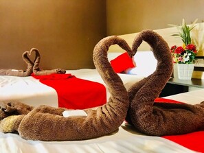 A hotel room with two beds, one with a red blanket and a heart-shaped towel arrangement.