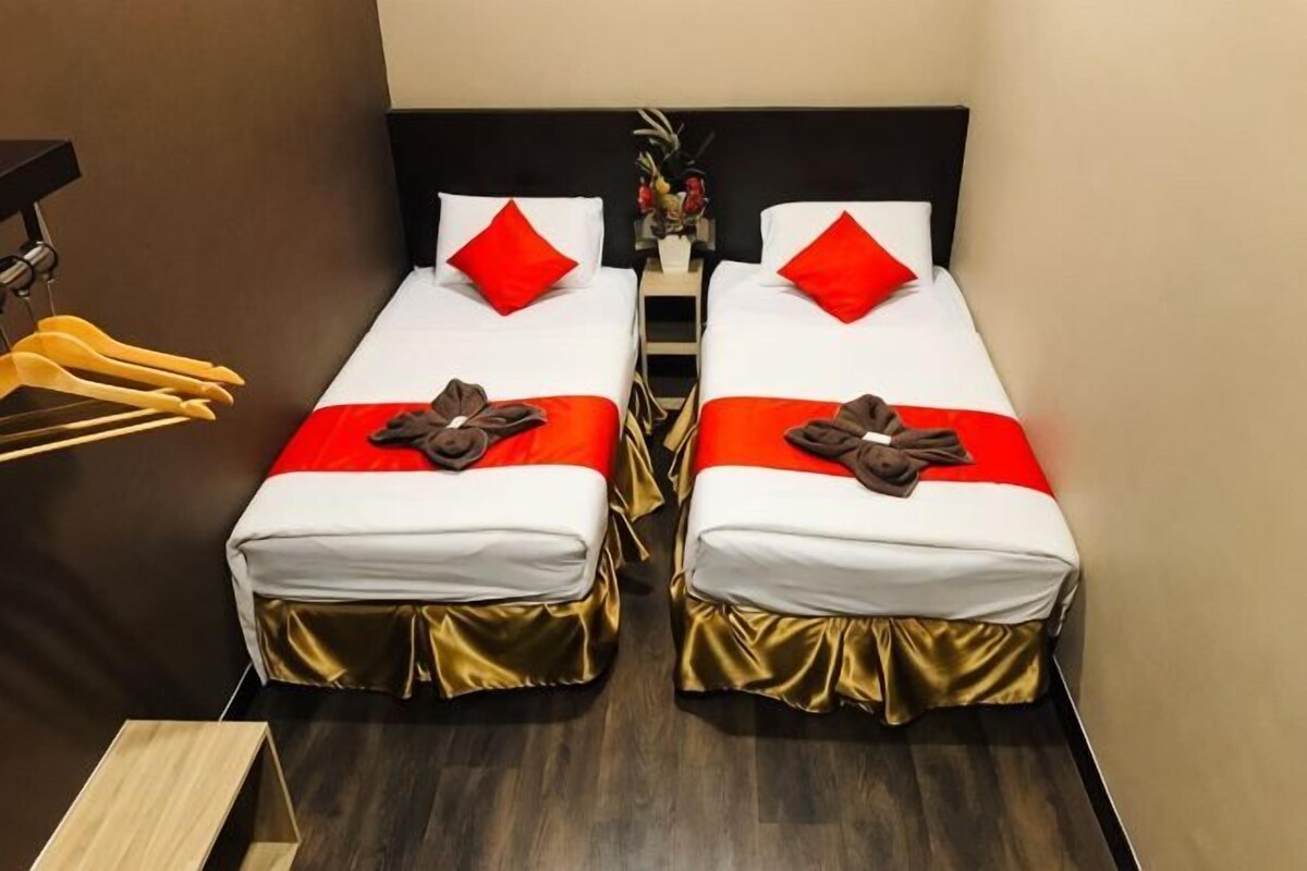 Two single beds with red pillows, gold bed skirts, and a small table between them.