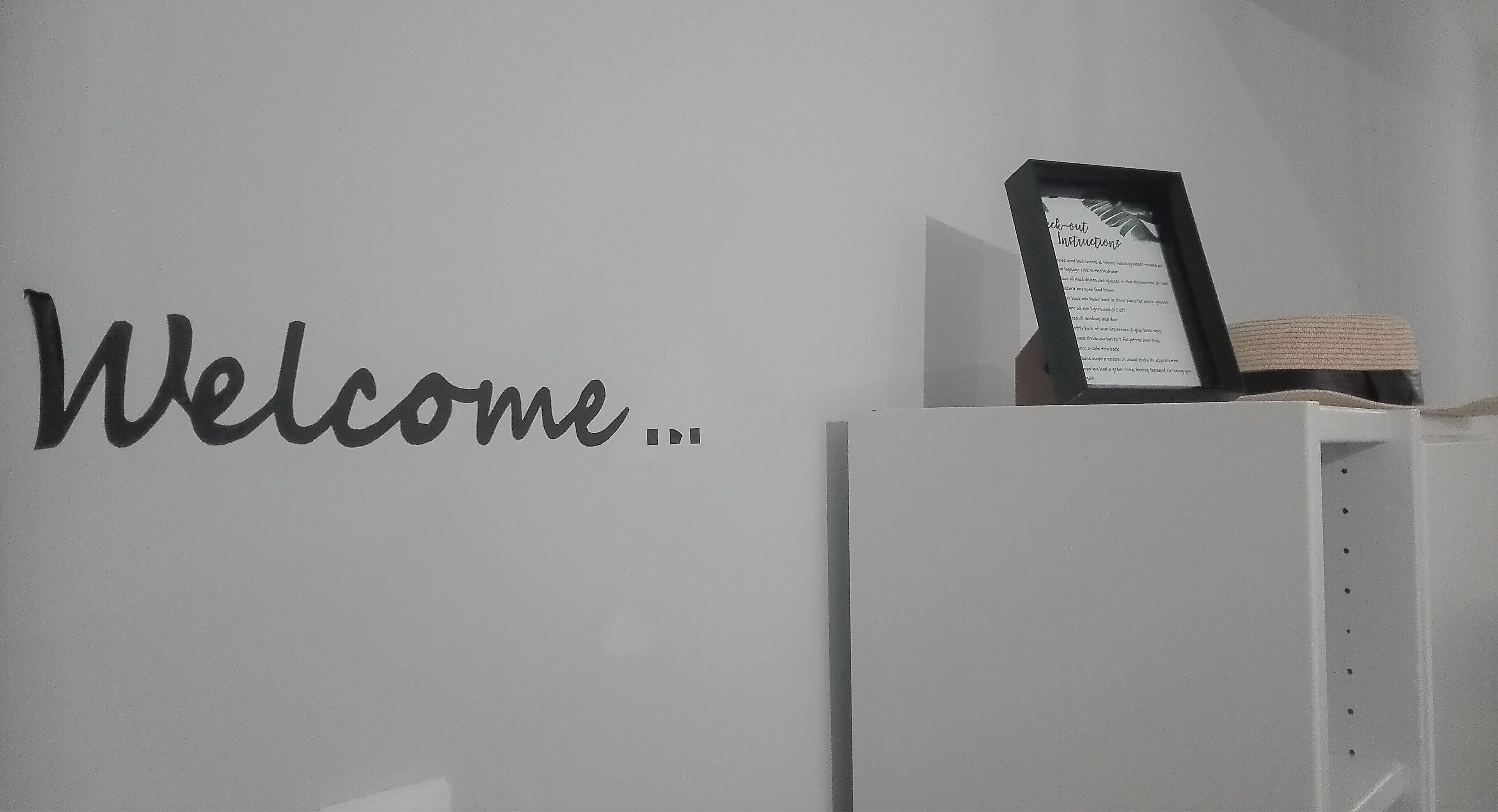 A wall with the word "Welcome..." and a framed document on a stand.