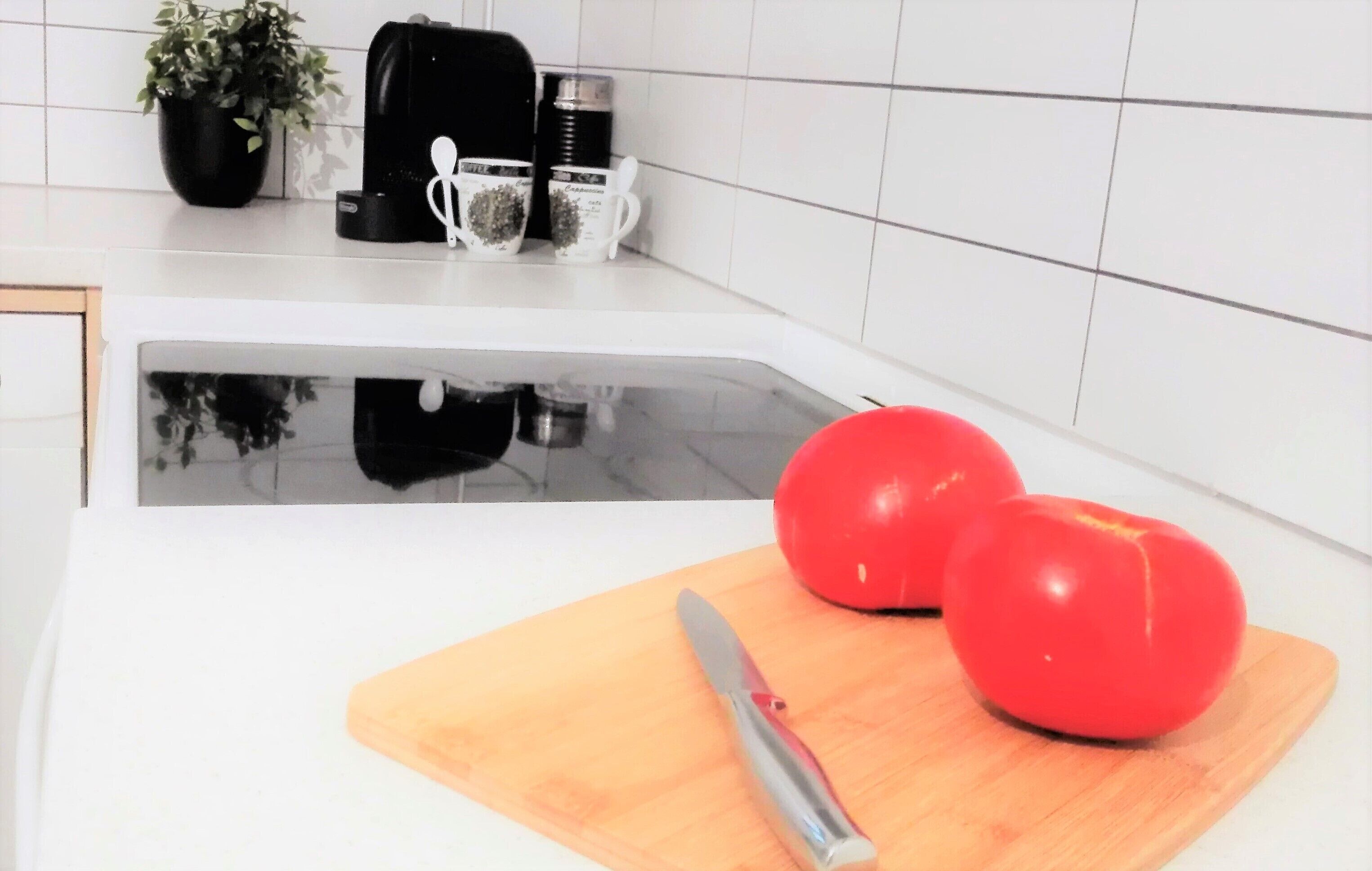 A kitchen with a white countertop, a wooden cutting board, a knife, and two tomatoes.