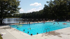 Une piscine où des gens nagent et se détendent, entourée d’arbres et bordée d’un lac.