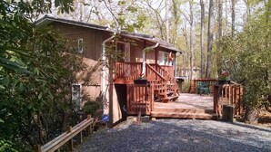 Une cabane en bois dotée d’un porche, d’un escalier et d’une allée en gravier, le tout entouré d’arbres.