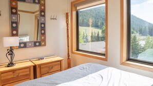 A bedroom with a bed, a dresser, a mirror, and a window with a mountain view. - 2800 Slopeside 2 Bedroom Condo by RedAwning (Keystone)