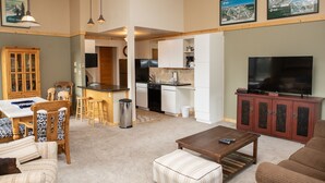 A spacious living room with a dining area, kitchen, and a TV on a cabinet. - 2800 Slopeside 2 Bedroom Condo by RedAwning (Keystone)