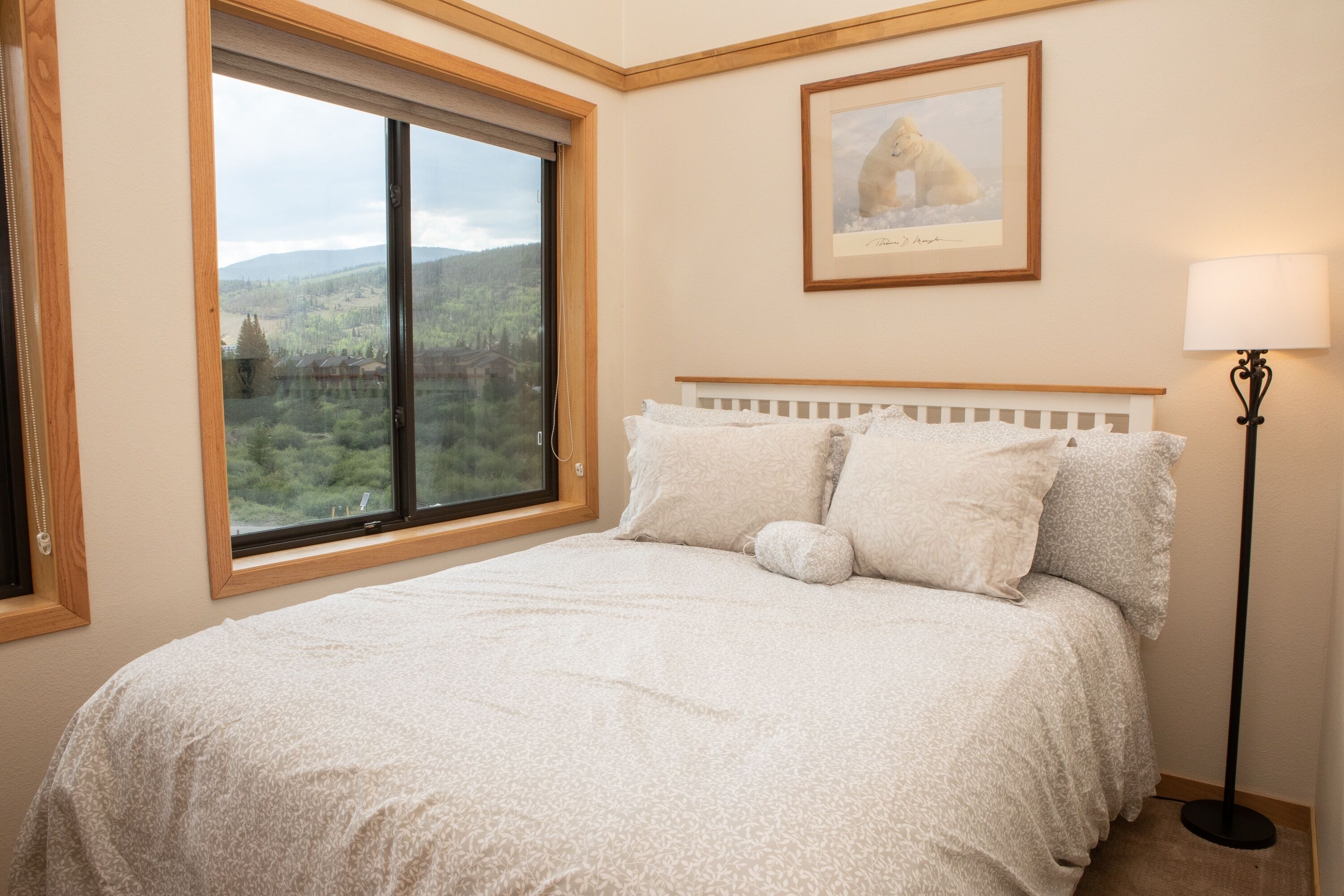 A bedroom with a large window offering a view of a forest and mountains.