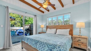 A bedroom with a bed, two bedside tables, a ceiling fan, a window with blinds, and a view of the outside. - Island Gem B 2 Bedroom Villa by RedAwning (Anna Maria)
