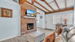 A living room with a brick fireplace, a mounted TV, and a cozy seating area with patterned cushions. - Island Gem B 2 Bedroom Villa by RedAwning (Anna Maria)