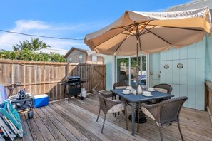 Eine Holzterrasse mit Tisch und Stühlen, einem Grill und einem Sonnenschirm.