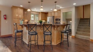 Una cocina con armarios de madera, una isla central con taburetes de bar, electrodomésticos de acero inoxidable e iluminación colgante.