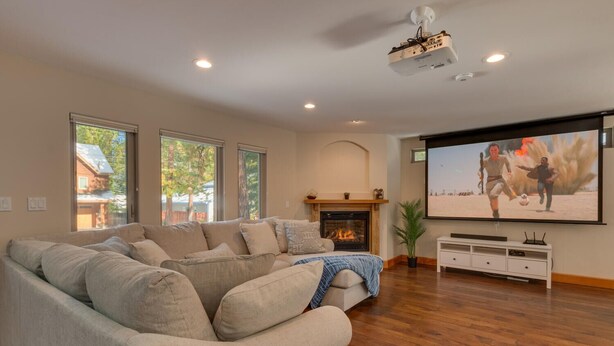 Una sala de estar con un amplio sofá modular, una chimenea, un televisor de pantalla plana y un proyector.