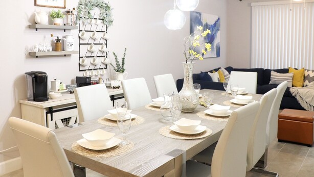 A dining area with a wooden table set for four, surrounded by white chairs. There are decorative items on the table, including a vase with yellow flowers. - FREE Early Check-In When Available! (Kissimmee)