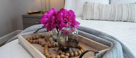 Una mesita de noche con una bandeja que sostiene un collar de cuentas, un recipiente de vidrio con flores y un quemador de aceite de latón.