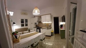 Una cocina compacta con armarios blancos, una mesa de comedor con sillas, una lámpara colgante y una pequeña encimera con una cafetera.