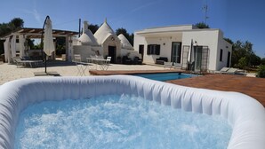 Una piscina inflable con superficie de agua azul transparente, rodeada por una zona de patio con sillones de descanso y un edificio blanco de diseño moderno al fondo.