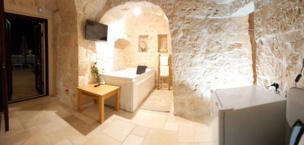 A stone-walled room with a sink, a wooden table, and a television mounted on the wall.