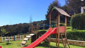 Ein Spielplatz mit einer roten Rutsche, Klettergerüsten und einer hölzernen Schutzhütte.