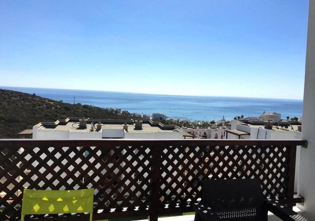 A balcony with a view of the sea and buildings in the distance.