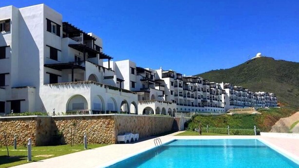 A modern hotel with a swimming pool, white and black architecture, and a view of a hill.