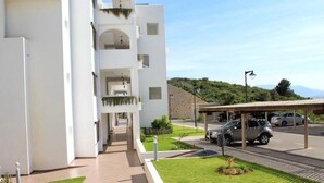 A modern building with a covered walkway, a parking area, and a view of a hilly landscape.