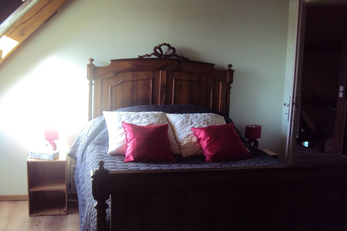 Un dormitorio con estructura de cama de madera, colcha acolchada y dos almohadas rojas.
