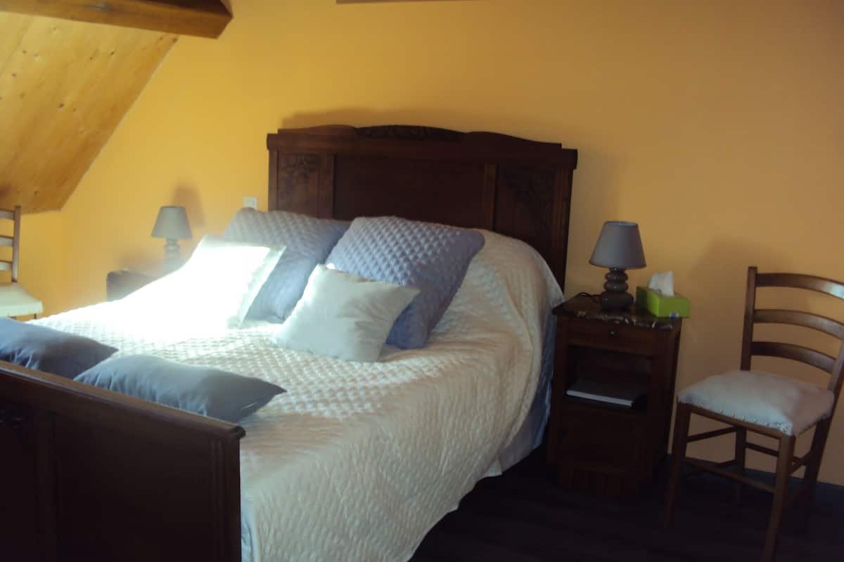 Un dormitorio con una cama de madera, una mesita de noche con una lámpara y una silla.