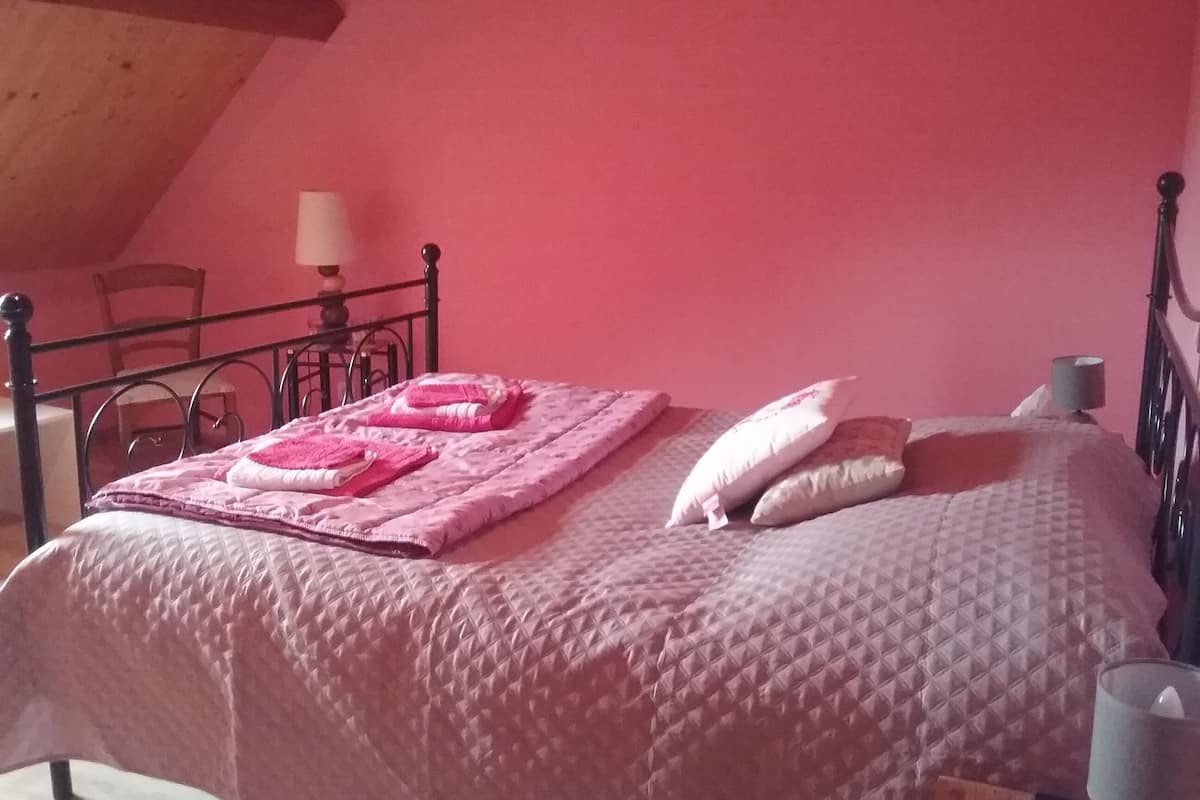 Un dormitorio con cama, almohadas, lámpara y una silla.