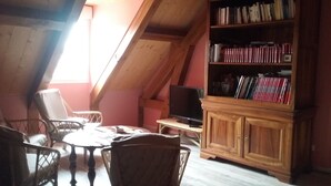 Una habitación acogedora en el ático con techo de madera, una estantería llena de libros, un televisor y dos sillones de mimbre alrededor de una pequeña mesa.