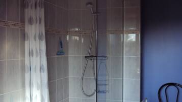 A shower area with a glass door, a showerhead, and a handrail.