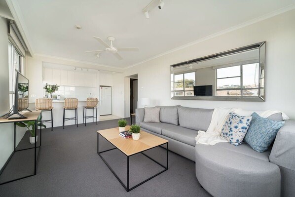 A modern living room with a grey sofa, a coffee table, and a large mirror. - Harbourside #49 (McMahons Point)