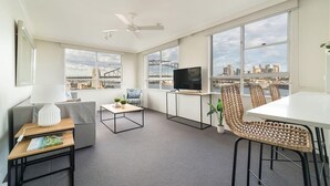 Un salon moderne comprenant un canapé, une table basse, un téléviseur posé sur un meuble et un coin repas avec des chaises.