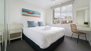 Une chambre d’hôtel équipée d’un lit, d’un bureau, d’une chaise, d’une fenêtre donnant sur la ville et d’un ventilateur de plafond.