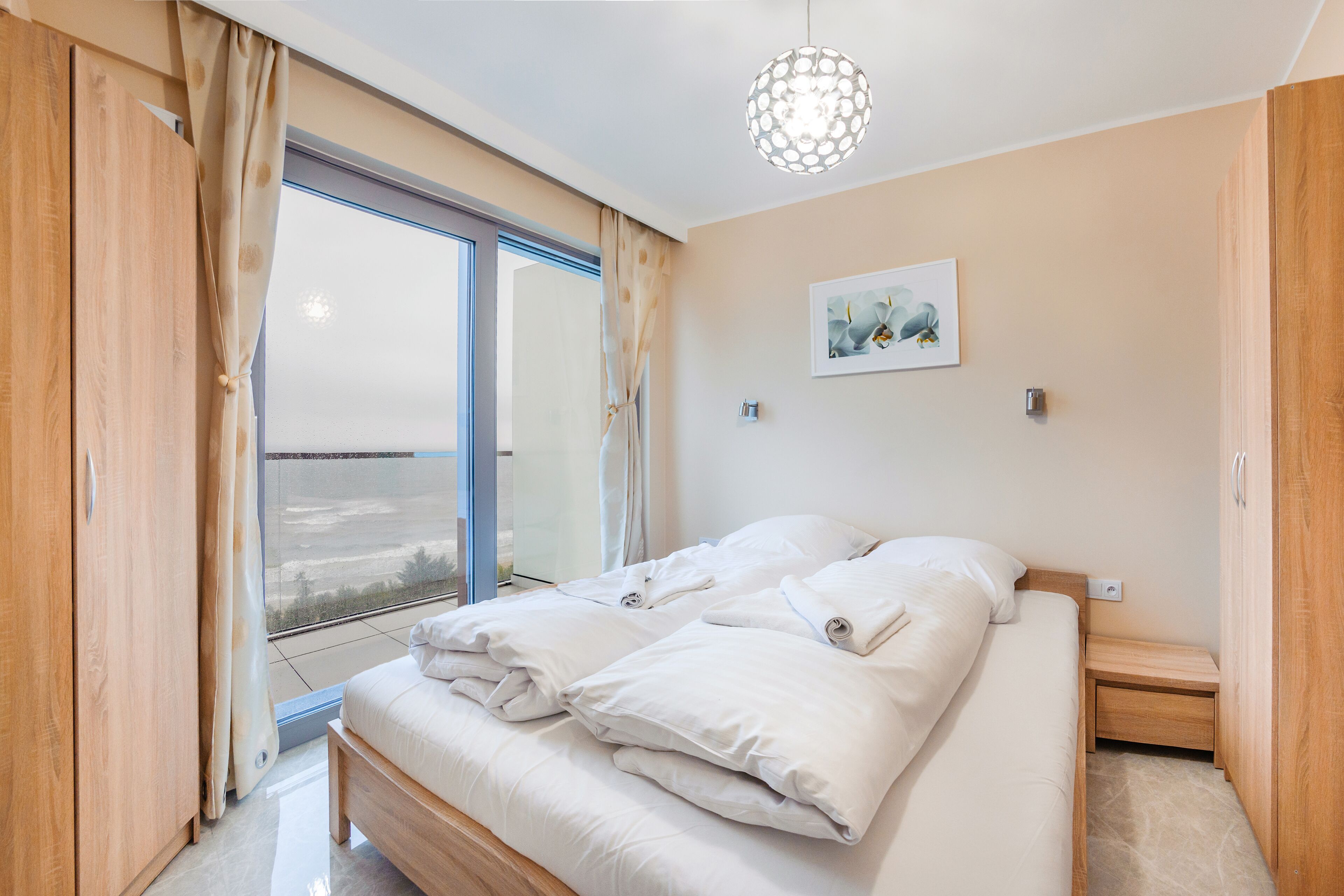 A bedroom with a large bed, wooden wardrobe, and a view of the outdoors through a sliding door.