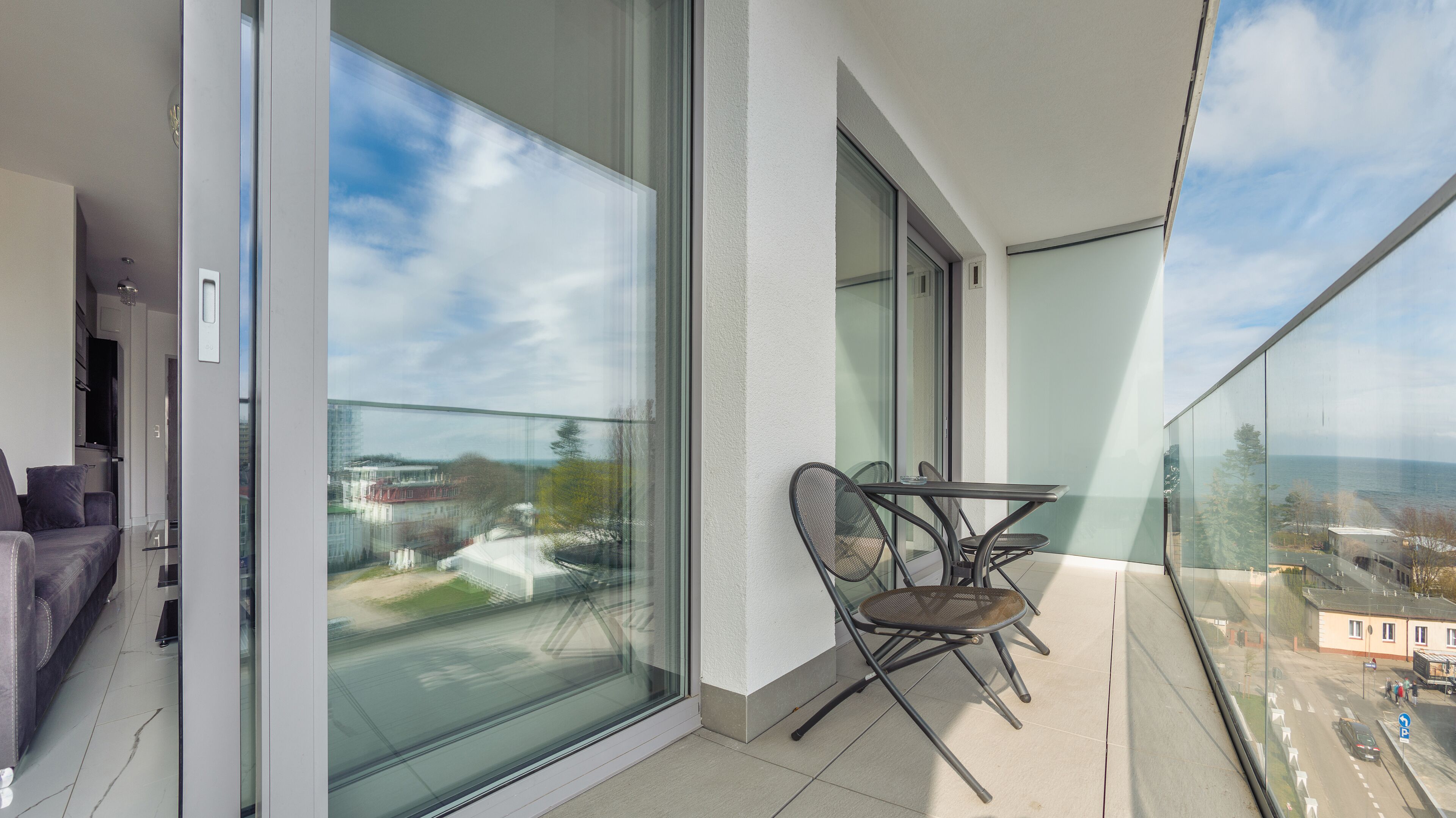 Un balcón con puerta de cristal, una mesa con sillas y vista a la ciudad.