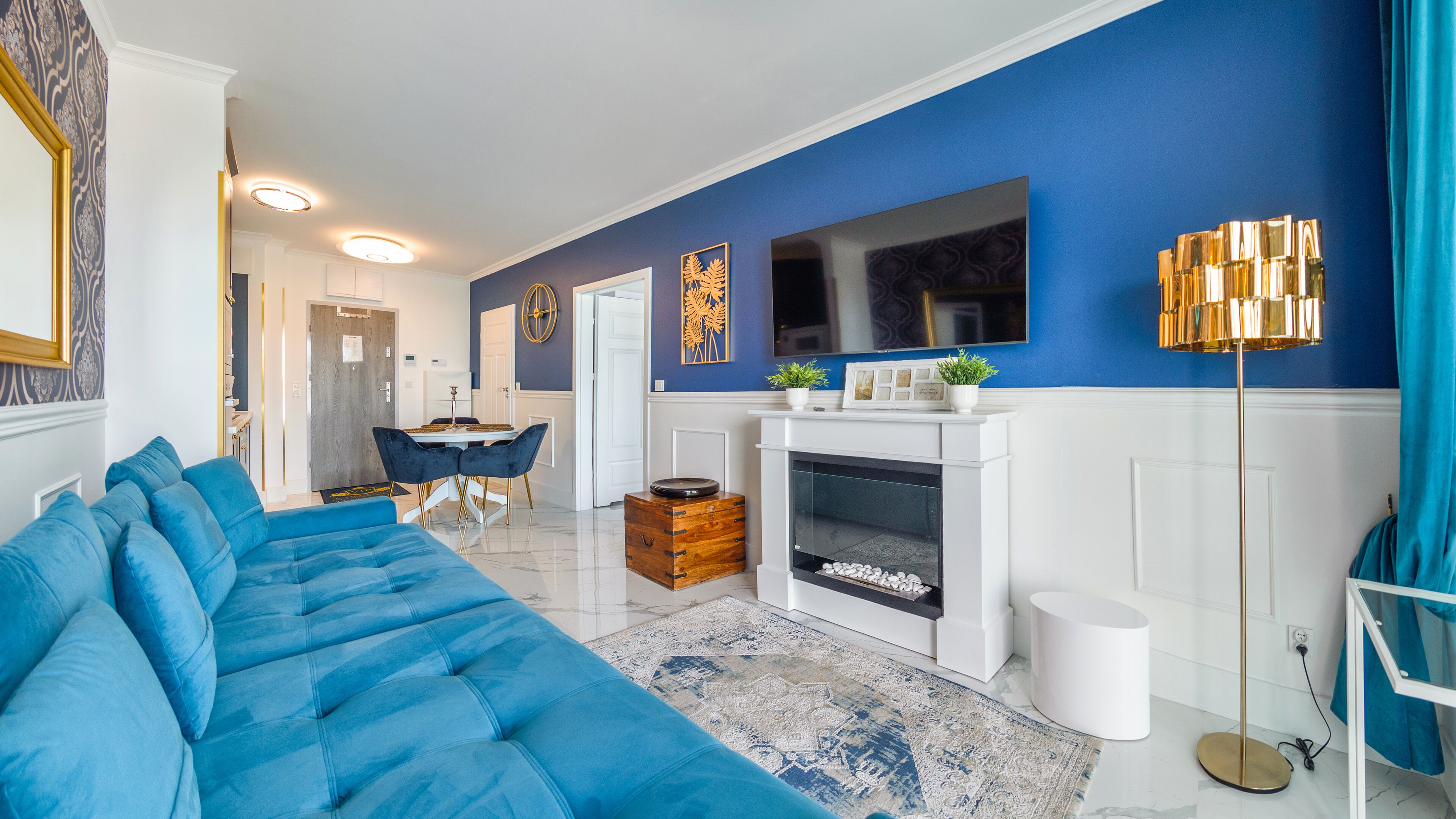 Ein modernes Wohnzimmer mit einem blauen Sofa, einem Kamin und einem Essbereich mit Tisch und Stühlen.