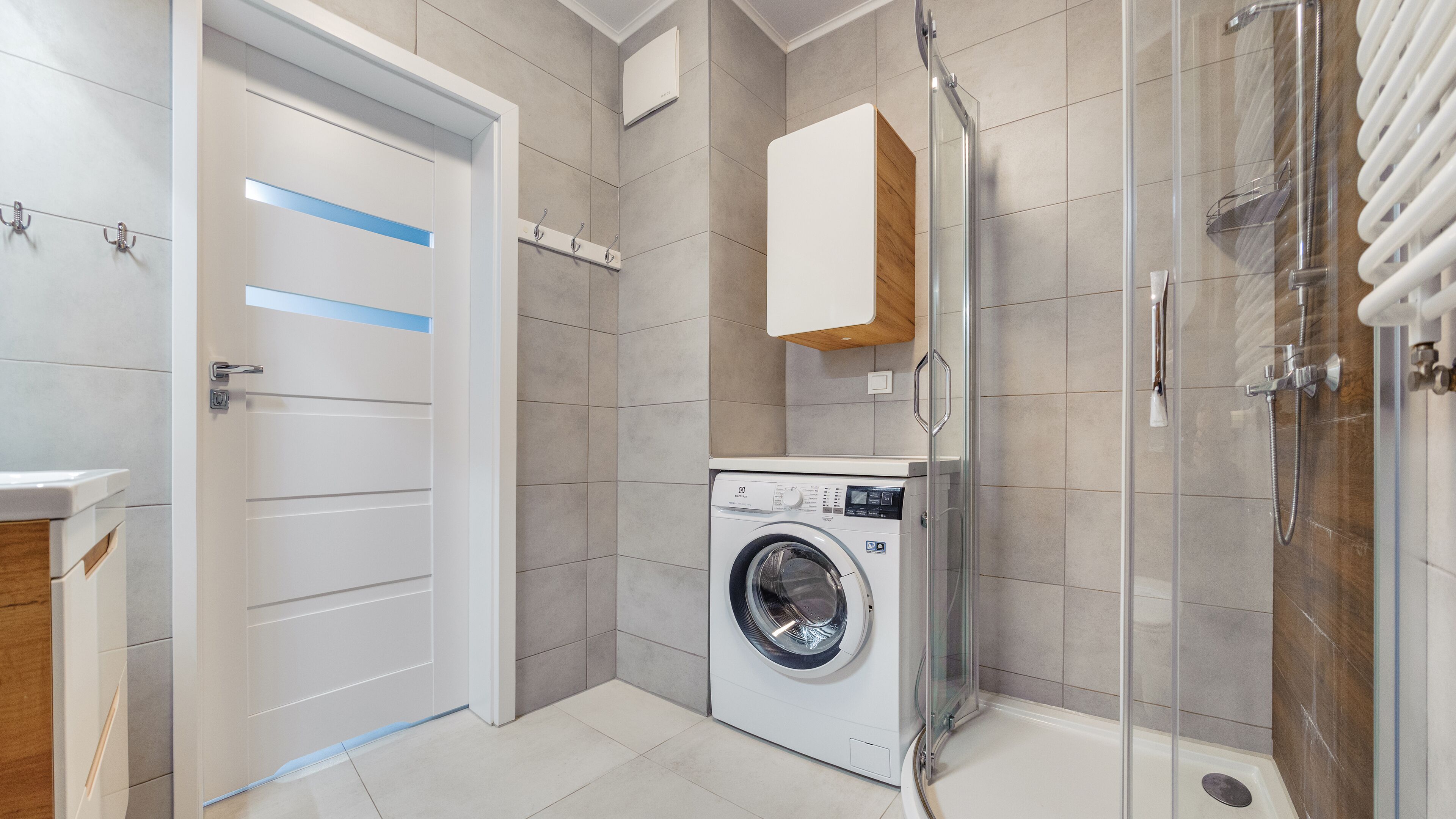 Une salle de bain moderne équipée d’un lave-linge, d’une douche à parois de verre et d’un meuble en bois.
